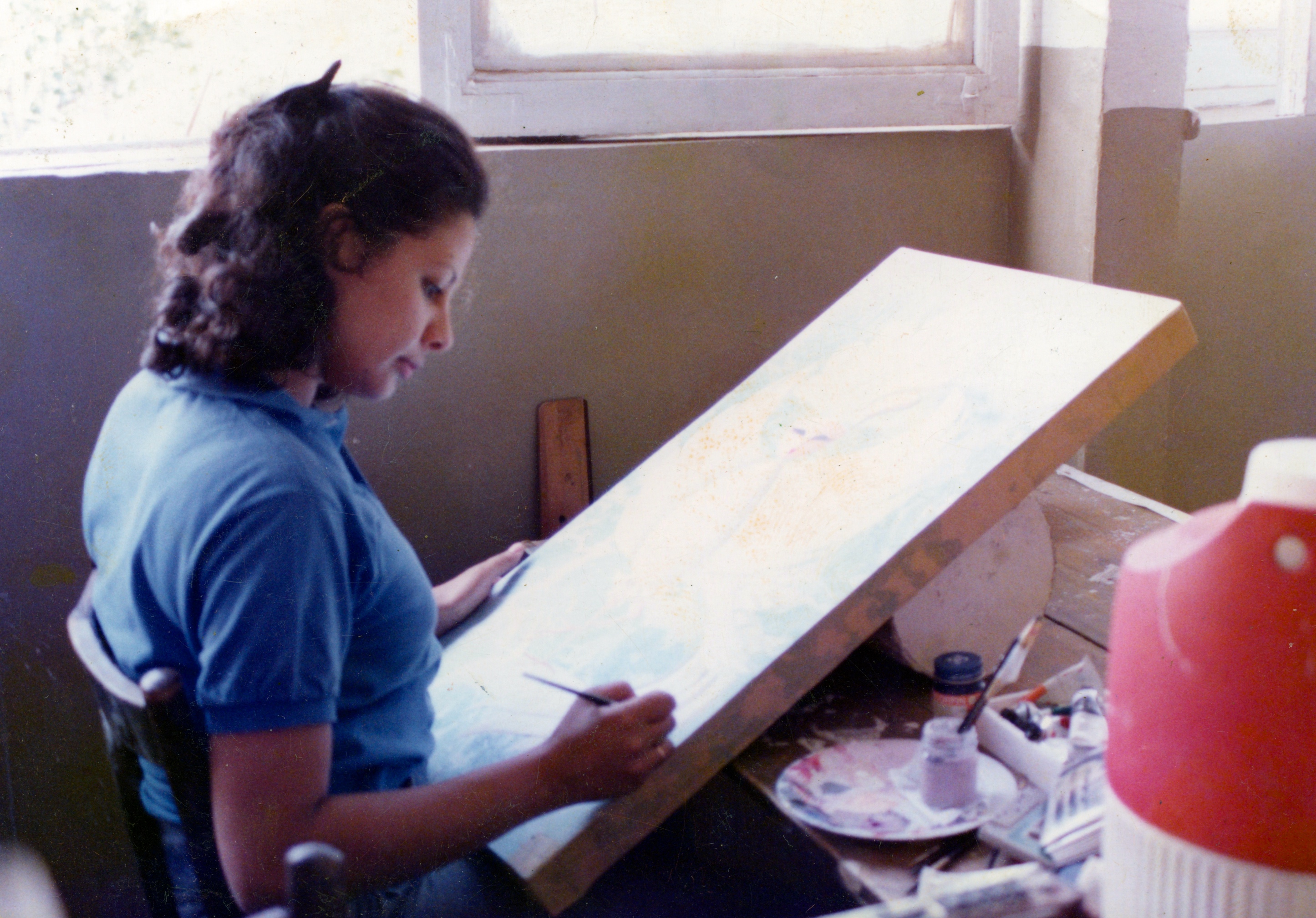 Ghada drawing at her work table with a brush and palette